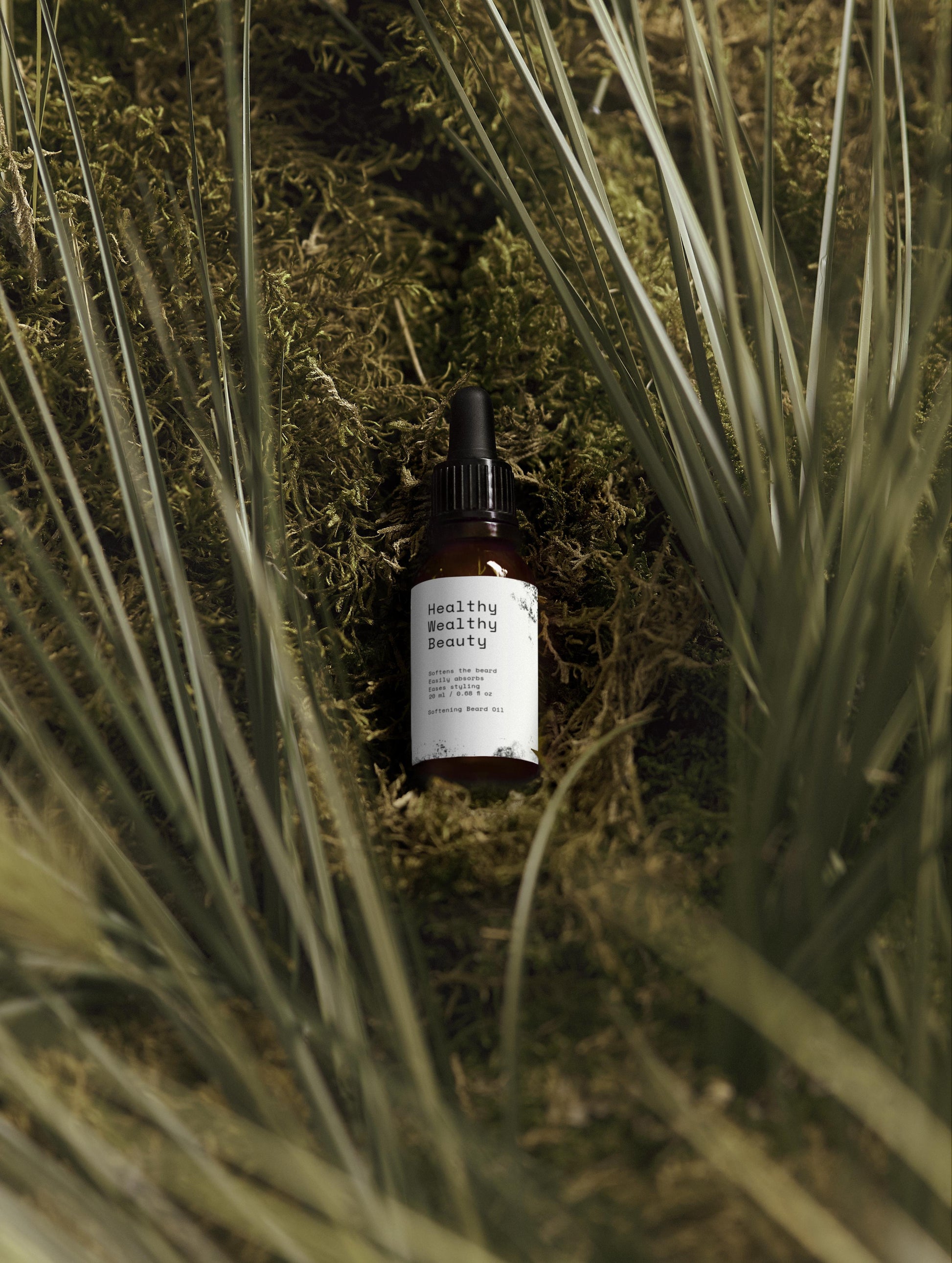 Softening Beard Oil bottle in amber packaging placed on mossy ground surrounded by grass blades.